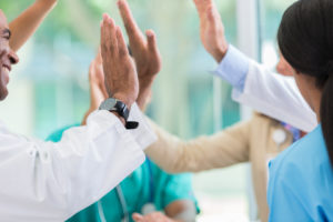 Five medical professionals standing in a circle giving each other high fives